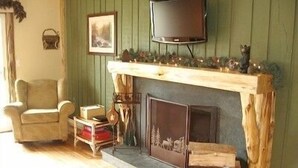 Una sala de estar acogedora con chimenea, un televisor montado encima y un sillón cómodo.