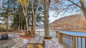 A wooden deck with picnic tables and benches overlooking a body of water, surrounded by trees and a wooden fence.
