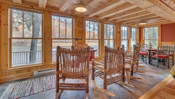 A wooden interior with large windows, rocking chairs, and a dining area.