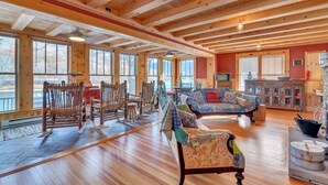 A spacious living room with wooden floors, large windows, a fireplace, and rustic furniture.