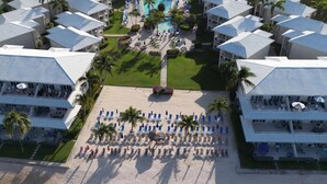 Vista aérea de un complejo turístico con varias edificaciones, una playa con sombrillas y una zona de piscina.
