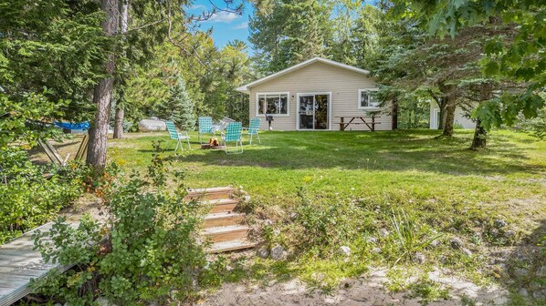 A house with a covered patio, a lawn, and a wooden deck. - Perfect Lakefront Family Cabin, 2 Kayaks Included! (Interlochen)