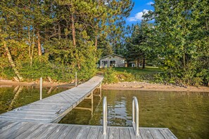 A wooden dock leading to a house surrounded by dense trees and a calm body of water. - Perfect Lakefront Family Cabin, 2 Kayaks Included! (Interlochen)