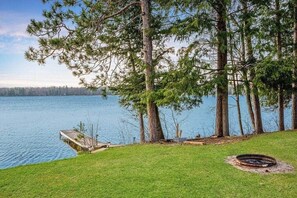 A lakeside property with a grassy area, a wooden dock, and a fire pit. - Perfect Lakefront Family Cabin, 2 Kayaks Included! (Interlochen)