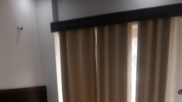 A neatly made bed with a headboard, a bedside table with a bottle, and a window with curtains.