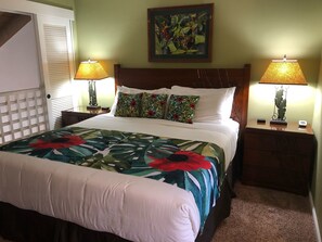 A neatly made bed with a floral bedspread, two bedside lamps, a nightstand with a clock, and a framed picture on the wall. - BEAUTIFUL CONDO WITH AWESOME SUNSET VIEWS (Kihei)