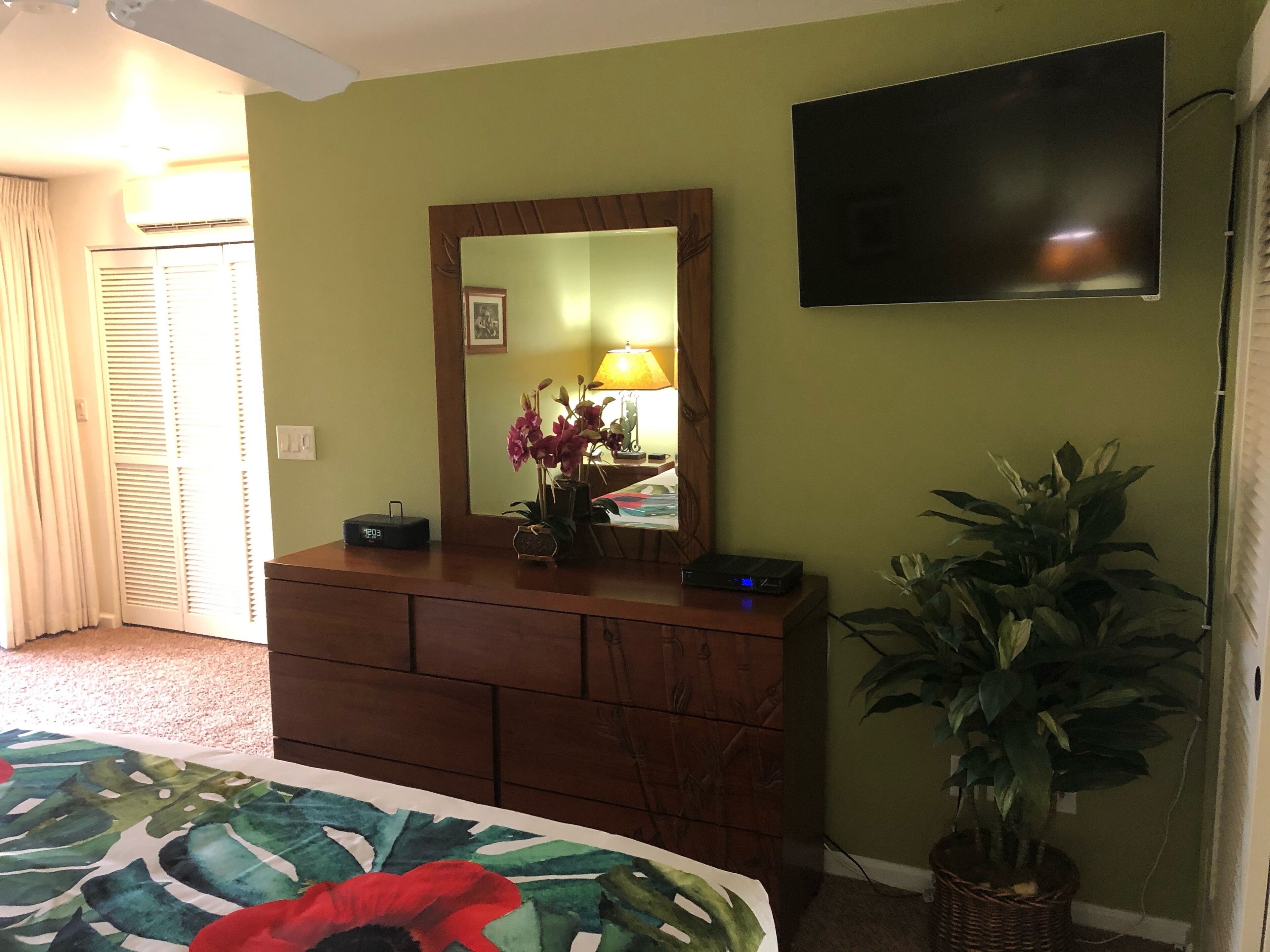 Ein Hotelzimmer mit Bett, Schminktisch, Fernseher, Spiegel, Lampe und einer Zimmerpflanze.