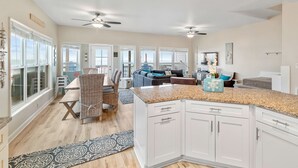 A spacious kitchen with white cabinets, granite countertops, and a dining area with wicker chairs and a patterned rug.