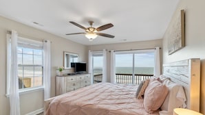 A bedroom with a bed, a ceiling fan, a TV, and a view of the ocean.