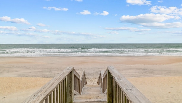 A wooden boardwalk leading to a beach with the ocean in the background.