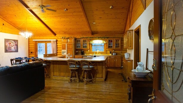 A log cabin interior with a dining area, kitchen, and bar seating.
