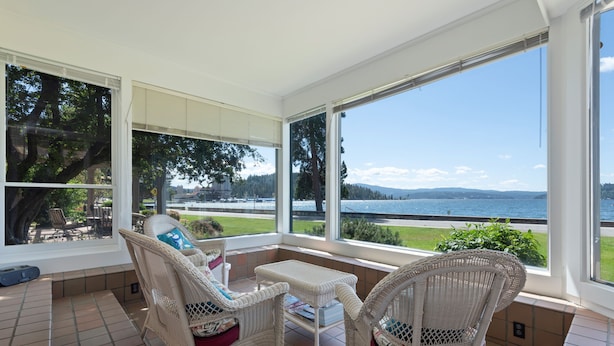 A sunlit patio with wicker furniture, large windows offering a view of a lake and distant mountains. - Premiere Beach House, Family Friendly, West Lakeshore Drive (coeur d'alene)