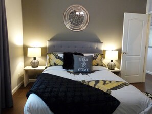 Een net opgemaakt bed met een zwart-wit beddekleed, twee bedlampen en een decoratief wandbord erboven.