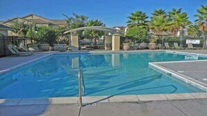 Une piscine rectangulaire à l’eau d’un bleu limpide, entourée de chaises longues et de palmiers.