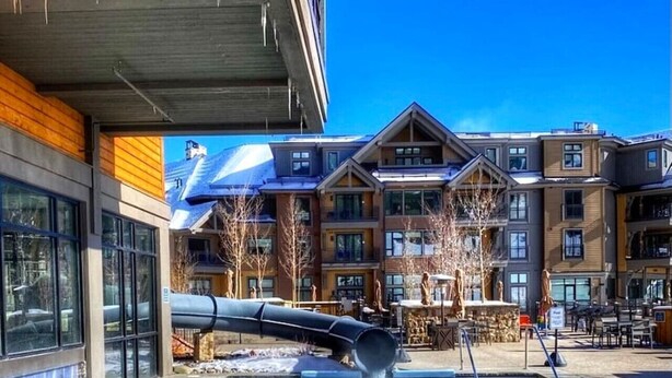 A pool with a water slide, surrounded by buildings with large windows and outdoor seating areas. - Luxury Ski-in/Ski-out residence (Breckenridge)