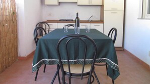 A dining area with a table set for four, surrounded by chairs, in a room with a kitchen in the background. - Camping Blumare Village (Furnari)