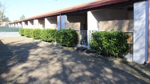 A row of single-story buildings with covered porches, each with a small entrance and a wooden fence. - Camping Blumare Village (Furnari)