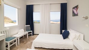 Habitación de hotel con cama, una silla, una mesita y vista al mar.