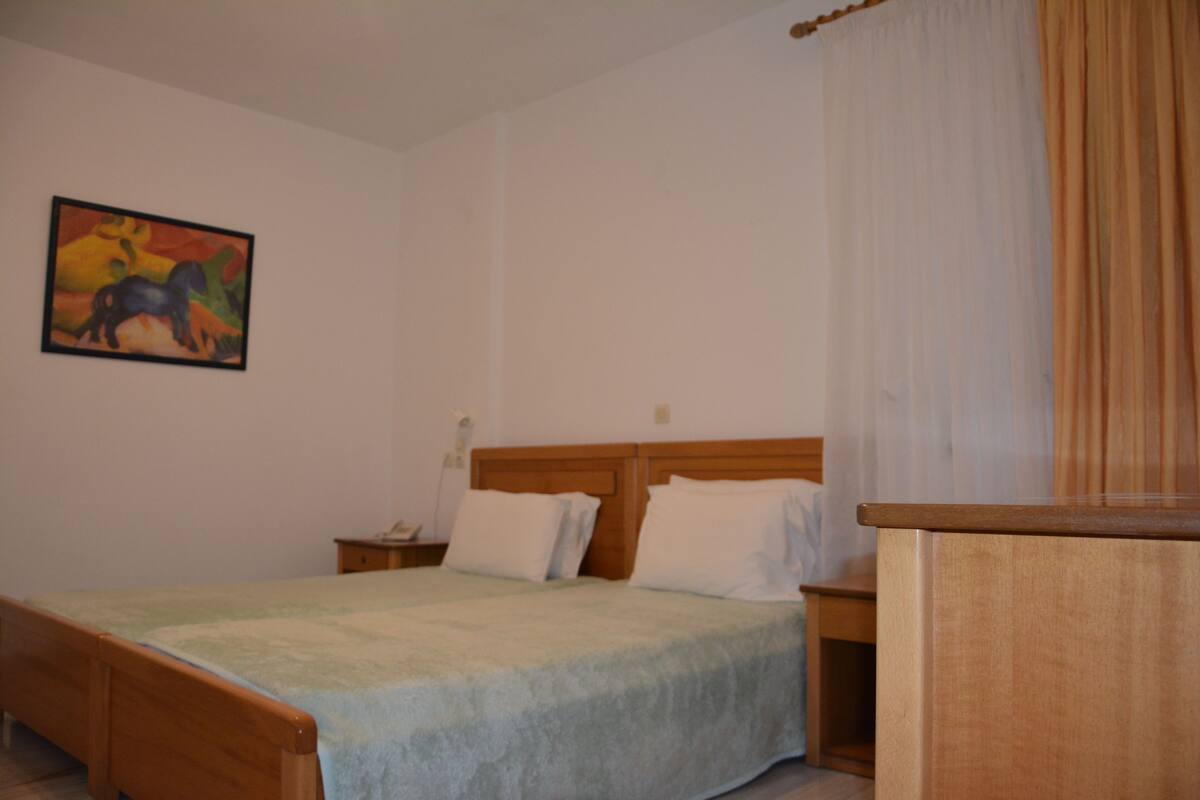 A bedroom with a wooden bed, a nightstand, a bedside table, and a painting on the wall.