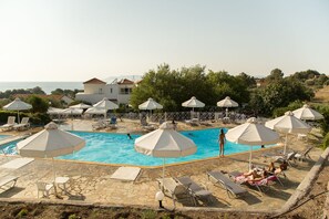 A pool area with umbrellas, lounge chairs, and a view of the sea. - Akti Hotel & Apartments (Lesvos)