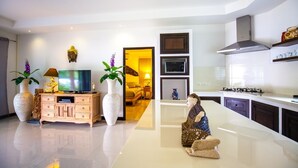 Una cocina moderna con horno integrado, microondas y estufa. Hay un armario de madera con un televisor encima. Una escultura decorativa está sobre la encimera de la cocina.