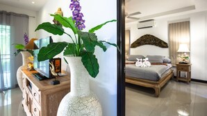 Una habitación de hotel con cama, mesita de noche, lámpara y un gran florero blanco con flores.