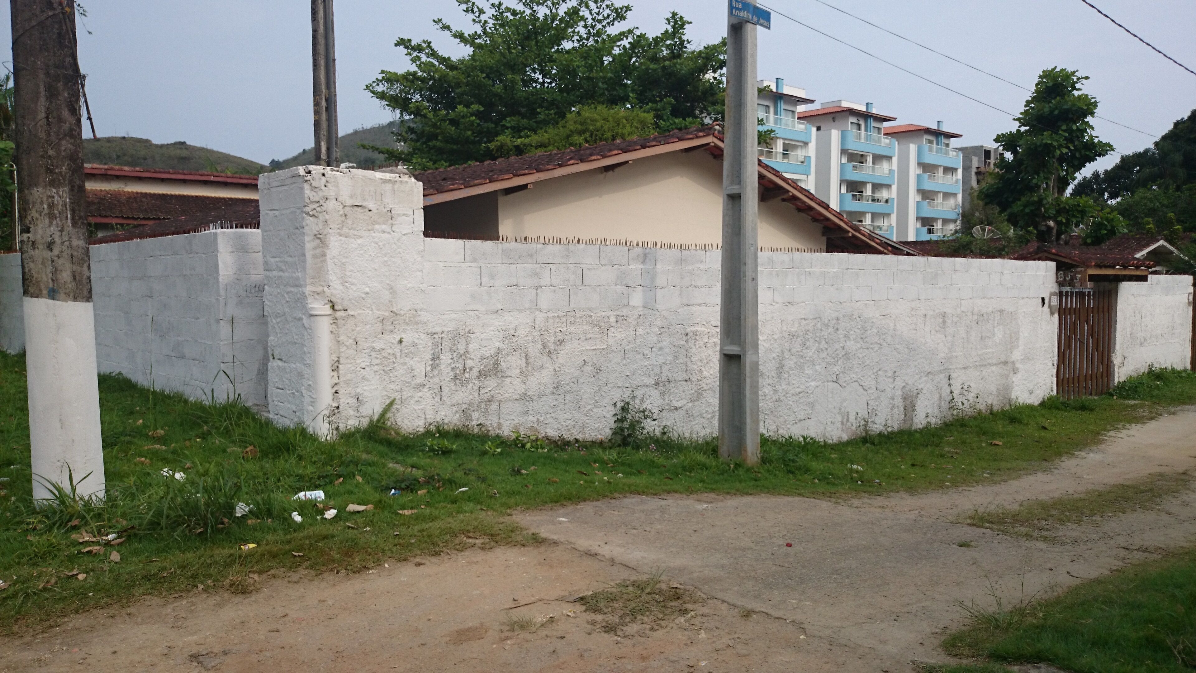 Un quartier résidentiel avec un mur blanc, un bloc de béton, un portail en métal et un bâtiment doté d’un toit rouge.