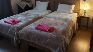 A hotel room with two beds, a nightstand, a lamp, and a wall-mounted picture. - Mary's mansion archontiko meteora (Kalabaka)