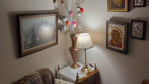 A room with a wooden side table, a lamp, a vase with branches and ornaments, and several framed pictures on the wall. - Mary's mansion archontiko meteora (Kalabaka)