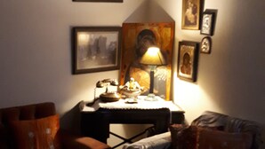 A dimly lit living room with a sofa, a table with a lace tablecloth, and a lamp. There are framed pictures on the wall and a small table with a lamp and decorative items. - Mary's mansion archontiko meteora (Kalabaka)