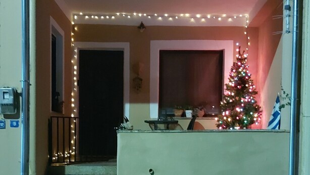 A building with a porch decorated with string lights and a Christmas tree. - Mary's mansion archontiko meteora (Kalabaka)
