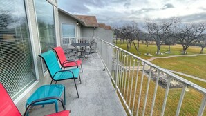Un balcón con una mesa y sillas, vista a un parque con árboles y un cielo nublado.