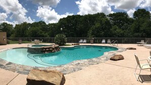 Una piscina con borde de piedra, sillas de descanso y un hogar a leña de piedra.