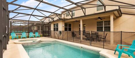 A covered outdoor swimming pool with turquoise chairs and tables, surrounded by a metal fence.