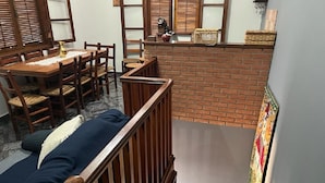 Een kamer met een eettafel, stoelen, een bank en een schouw met bakstenen.