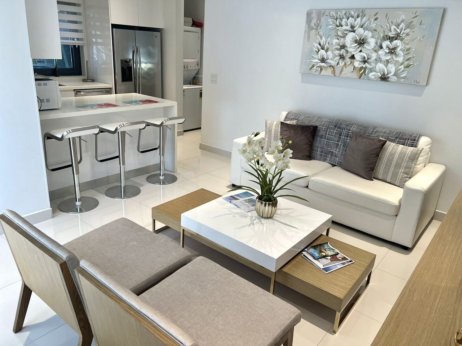 Un salon moderne avec un canapé blanc, une table basse et un coin repas équipé de tabourets de bar.