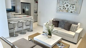 A modern living room with a white sofa, a coffee table, and a dining area with bar stools.