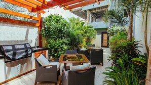 An outdoor patio with wicker furniture, a glass-top table, and a grill.