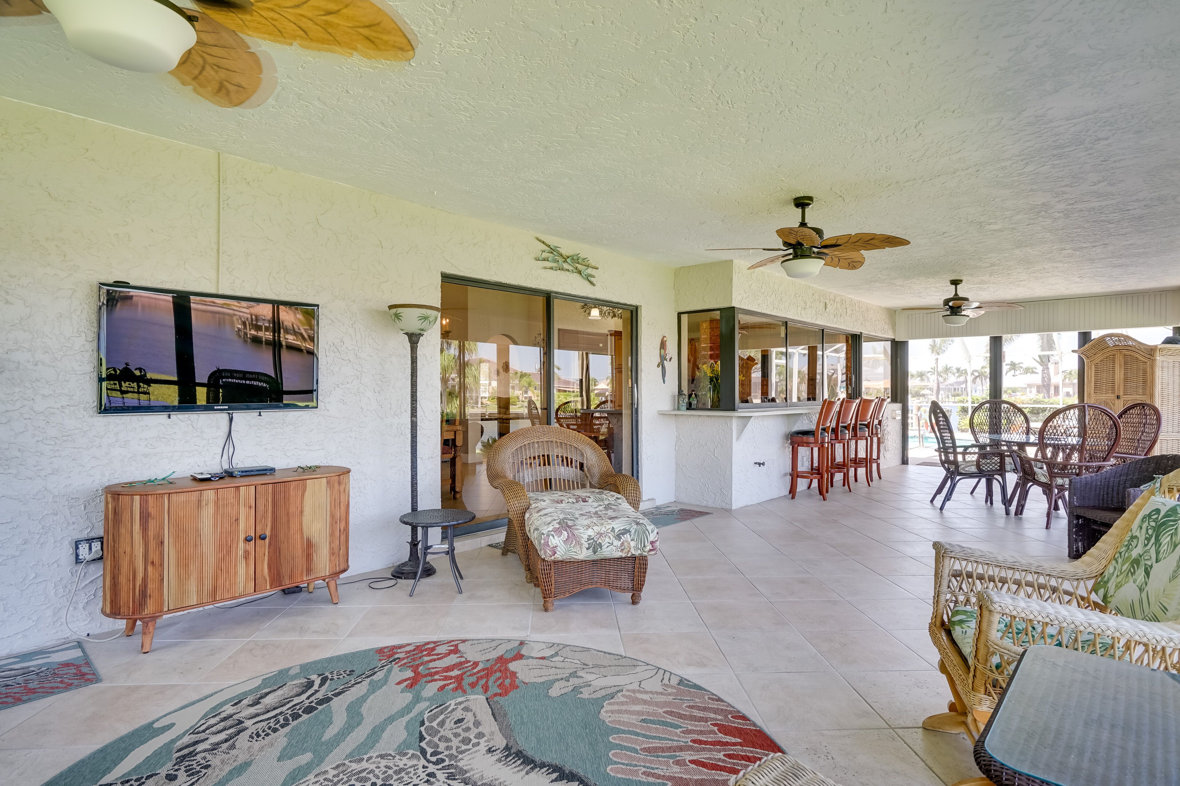 A spacious living area with a large TV, wicker furniture, and a ceiling fan.