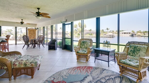 A spacious indoor area with wicker furniture, large windows, and a view of a body of water. - Private Dock: Canalfront Home in Cape Coral (Cape Coral)