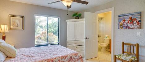 A bedroom with a bed, a ceiling fan, a window with blinds, a door leading to a bathroom, and a chair.