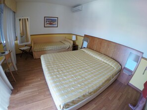 Une chambre d’hôtel avec un grand lit, un plus petit lit, un bureau, une chaise, un miroir et un tableau au mur.