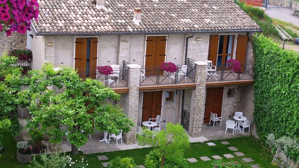A two-story building with a stone facade, wooden doors, and a balcony with white chairs and tables. - Hotel Romeo (Torri del Benaco)