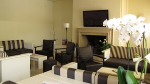 A hotel lobby with striped sofas, armchairs, a flat-screen TV, a fireplace, and white orchids. - Hotel Romeo (Torri del Benaco)