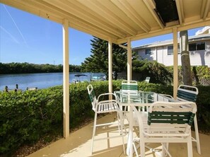 A covered patio with a table and chairs, overlooking a lake with boats and a house in the background. - Siesta Key Waterfront Condo, Fishing Pier, Pool - Short Walk to Turtle Beach! Cozy Cove 3 (Siesta Key)