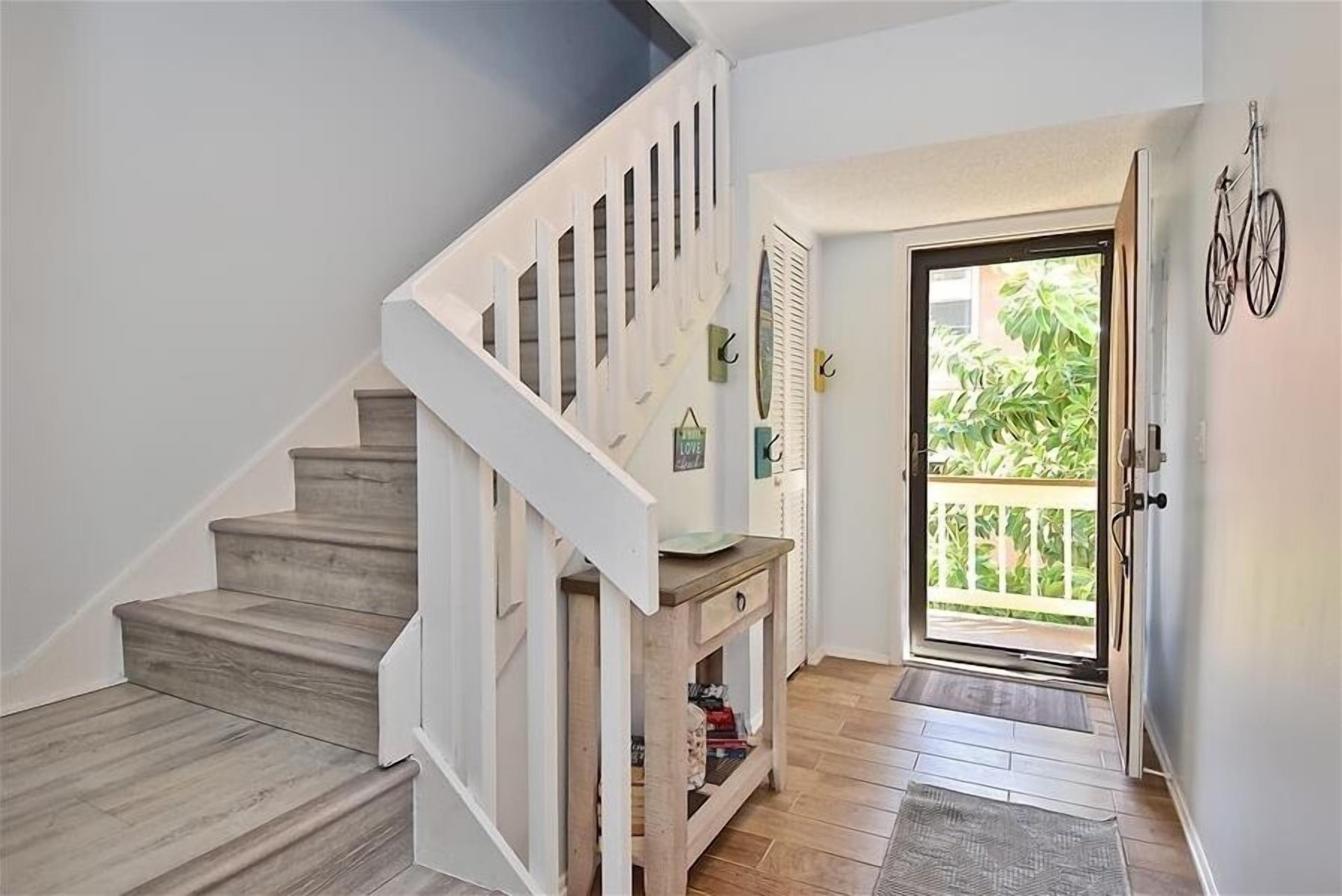 Eine Treppe mit Holzstufen und weißen Geländern, ein kleiner, hölzerner Konsolentisch und eine Tür zu einem Balkon mit Pflanzen.