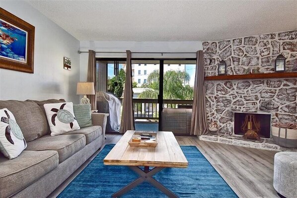 A living room with a sofa, coffee table, and stone wall fireplace. - Siesta Key Waterfront Condo, Fishing Pier, Pool - Short Walk to Turtle Beach! Cozy Cove 3 (Siesta Key)