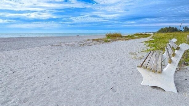 Une plage avec un banc en bois et un ciel dégagé.