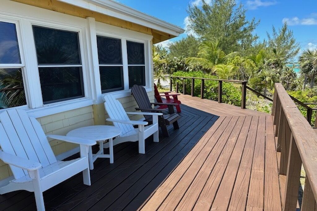 Una terraza de madera con sillas Adirondack blancas y una silla Adirondack roja.