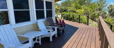 Una terraza de madera con sillas Adirondack blancas y una silla Adirondack roja.